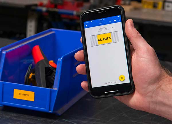 Wzór etykiety na ekranie z aplikacją Express Labels Mobile obok wydrukowanej etykiety. Obie mają żywy żółty kolor i napis „CLAMPS”.